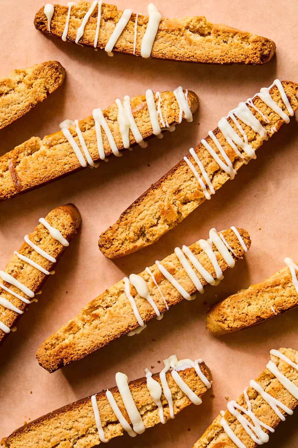 Eight gluten free almond flour biscotti cookies arranged on parchment paper, drizzled with white icing. The cookies are golden brown and have a crunchy texture.