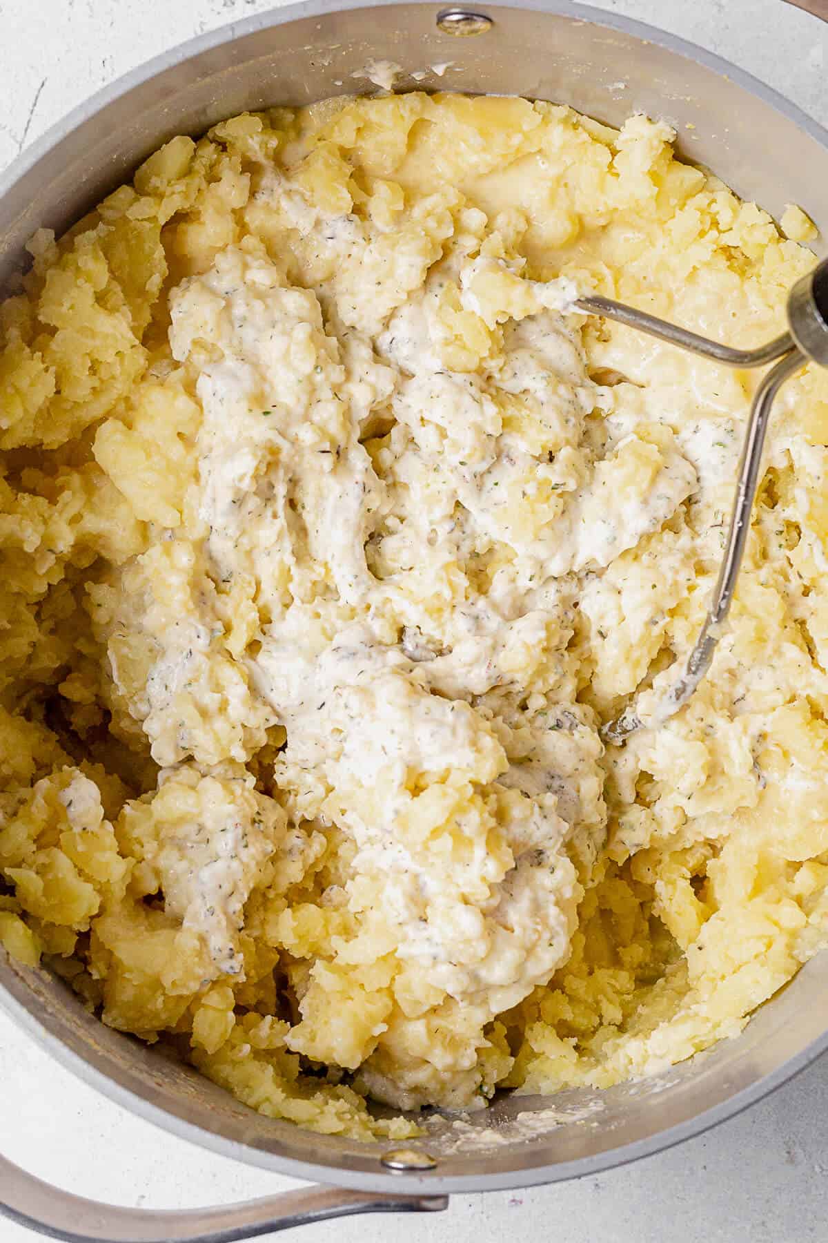 mashing potatoes in a pot with boursin cheese, milk, and butter.