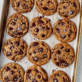 a tray of brown butter chocolate chip cookies with melted chocolate and flaky sea salt