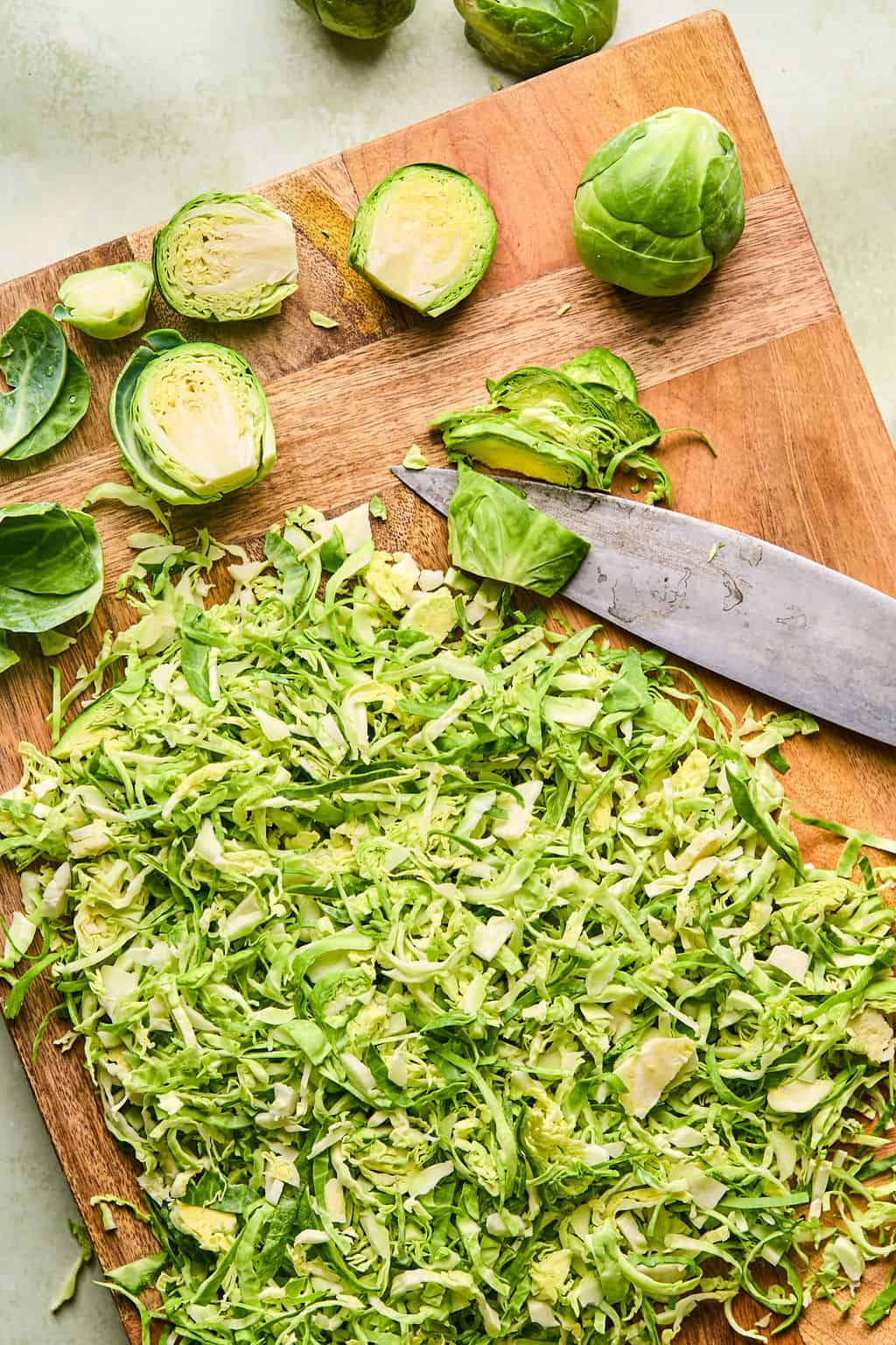 shredding brussels sprouts with a sharp knife on a cutting board.