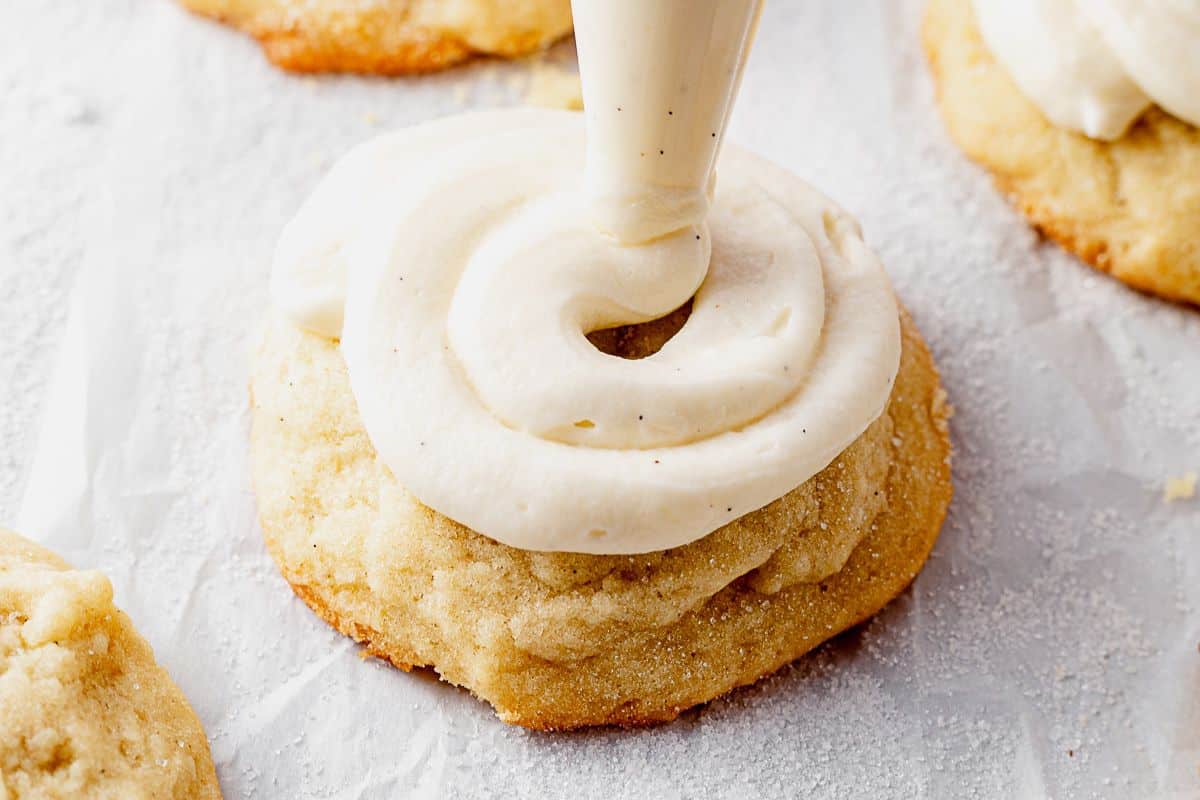 swirling cream cheese frosting on top of a vanilla almond cookie