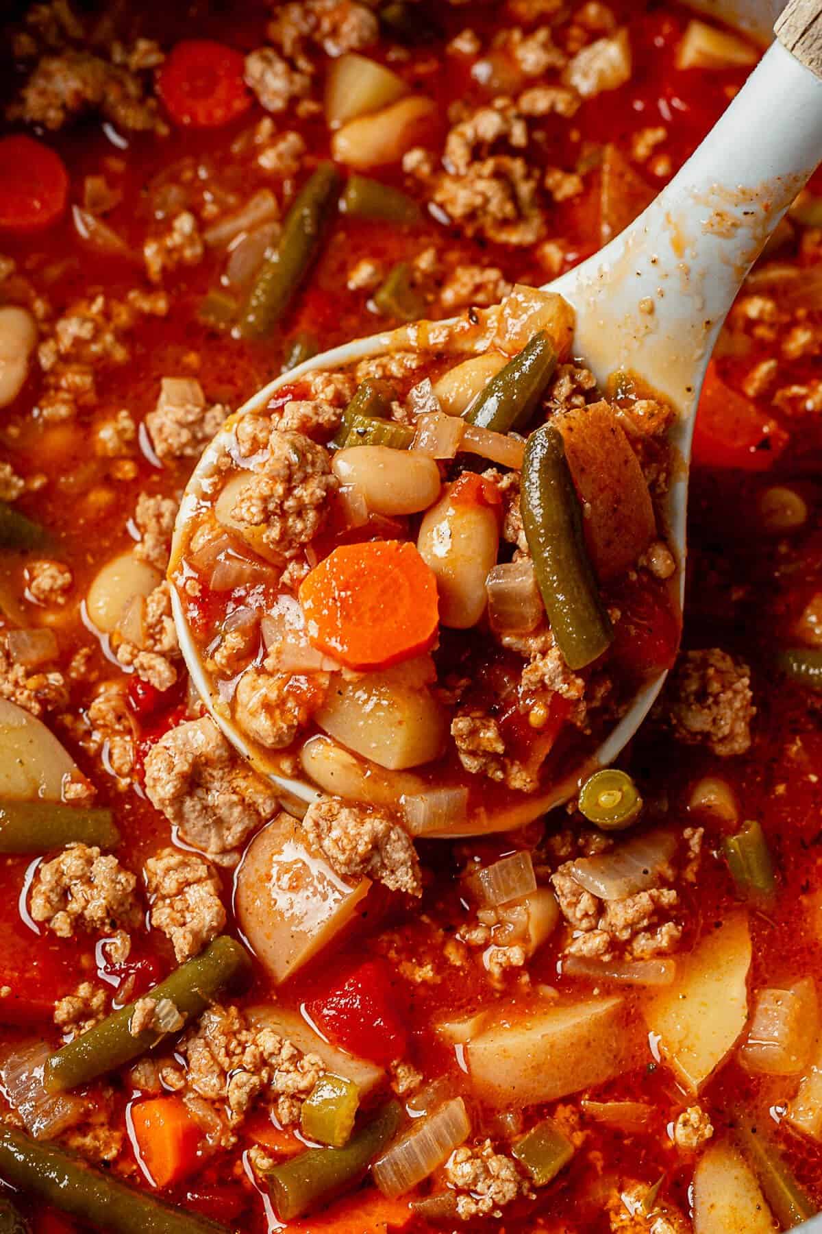 a ladle of ground turkey soup with carrots, potatoes, and green beans