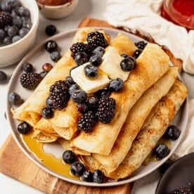 syrup dripping off of a stack of pancake roll ups with berries and butter