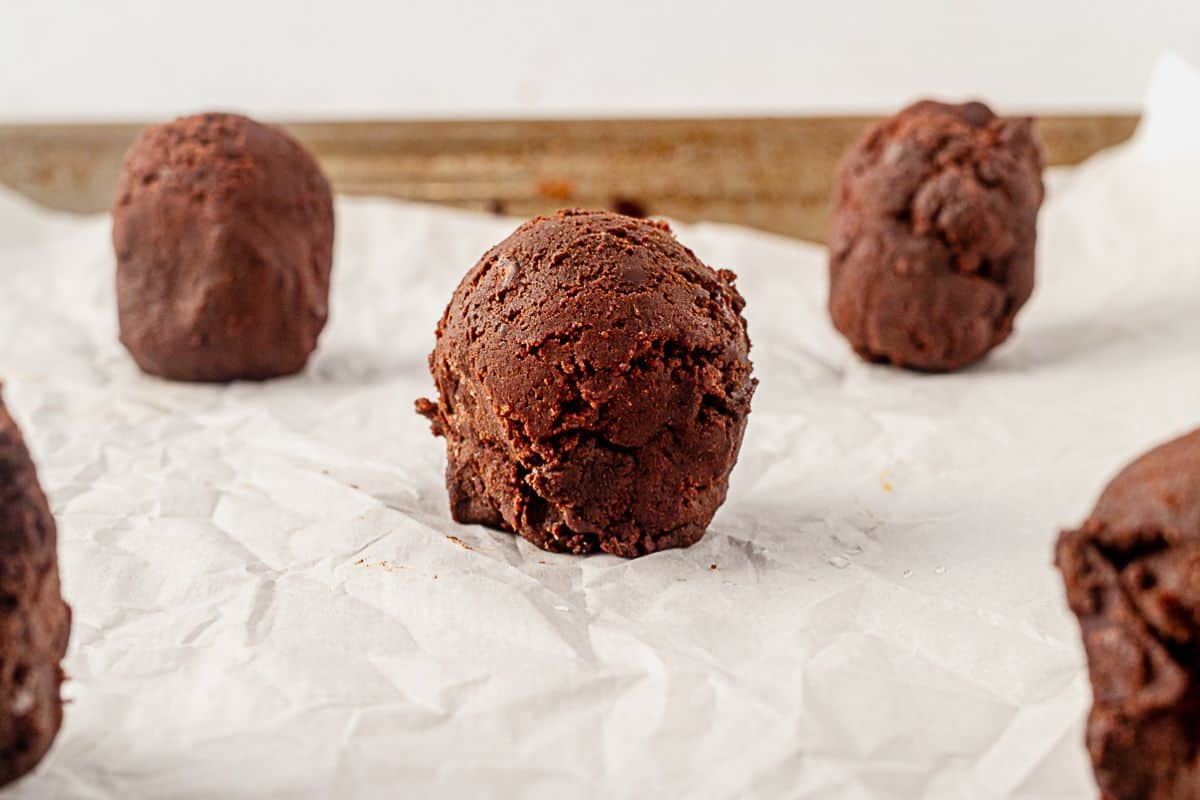 a tall scoop of chocolate cookie dough balls on a parchment lined baking sheet