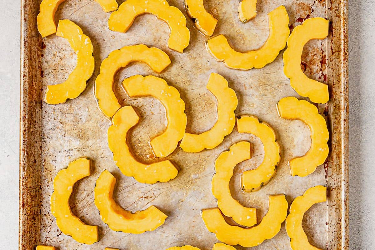 sliced delicata squash on a baking pan with olive oil and salt