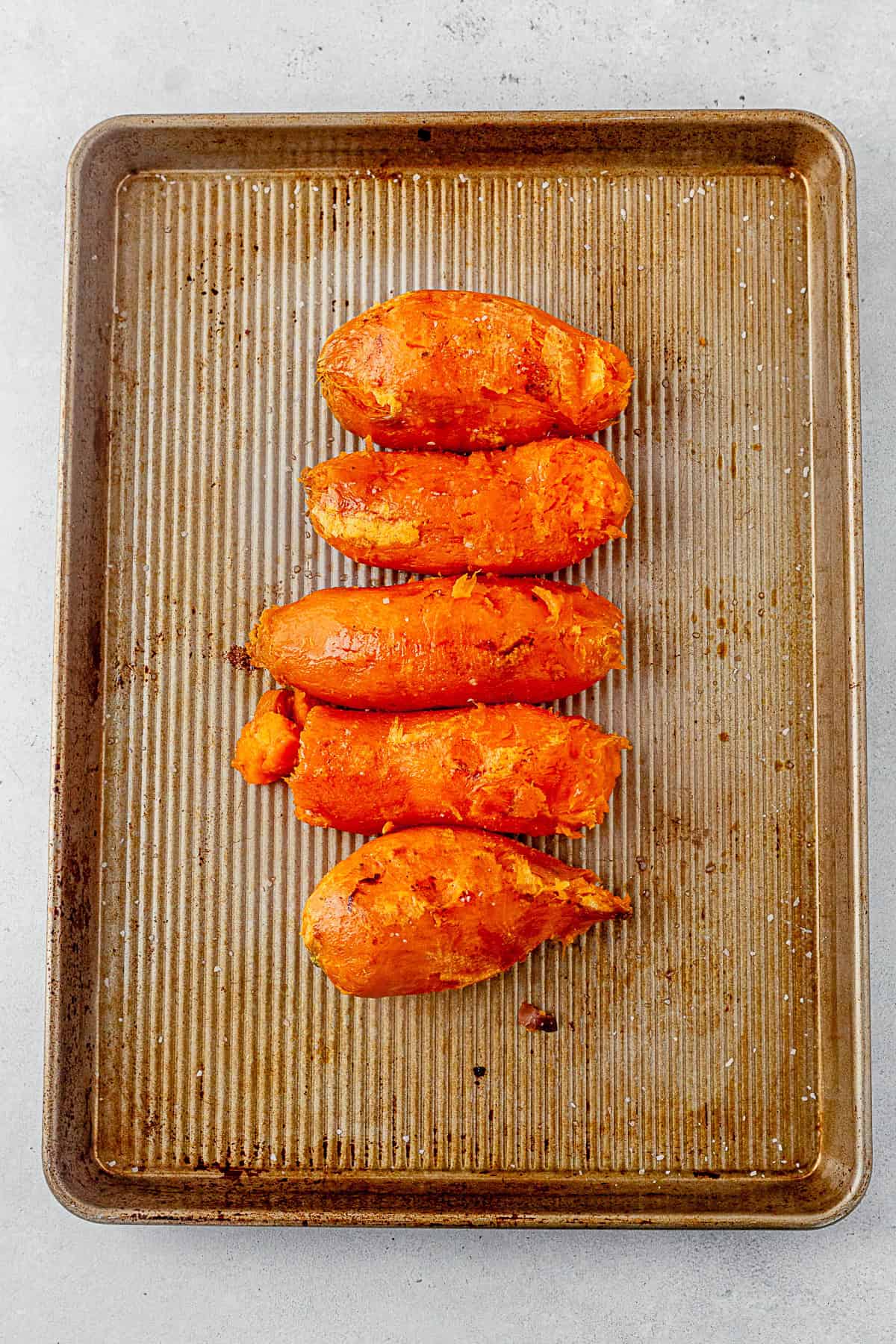 four roasted sweet potatoes with the skin removed on a baking sheet.