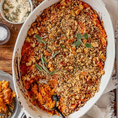 savory sweet potato casserole in a serving dish with a spoon and fresh sage