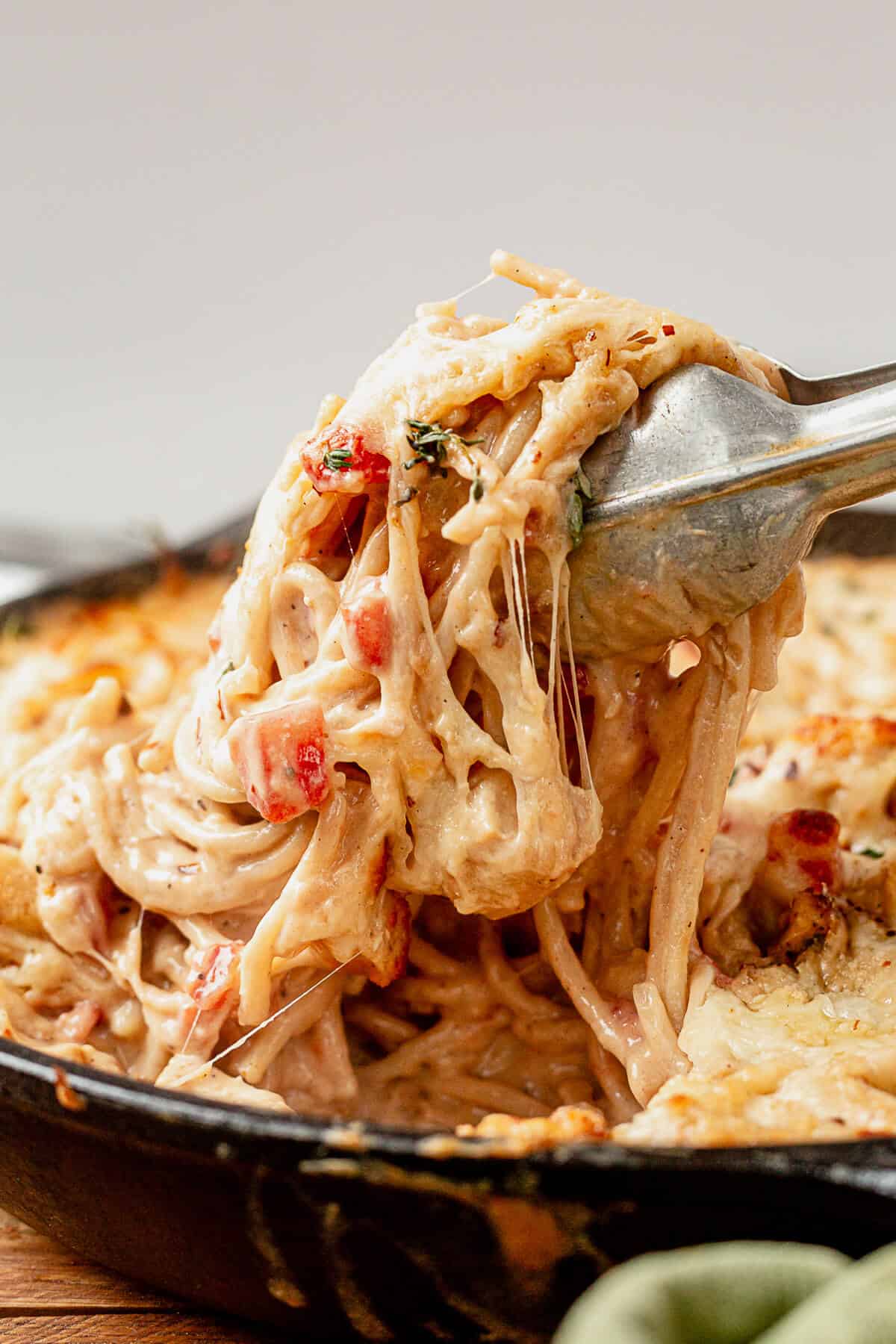 pulling cheesy creamy spaghetti chicken out of a skillet
