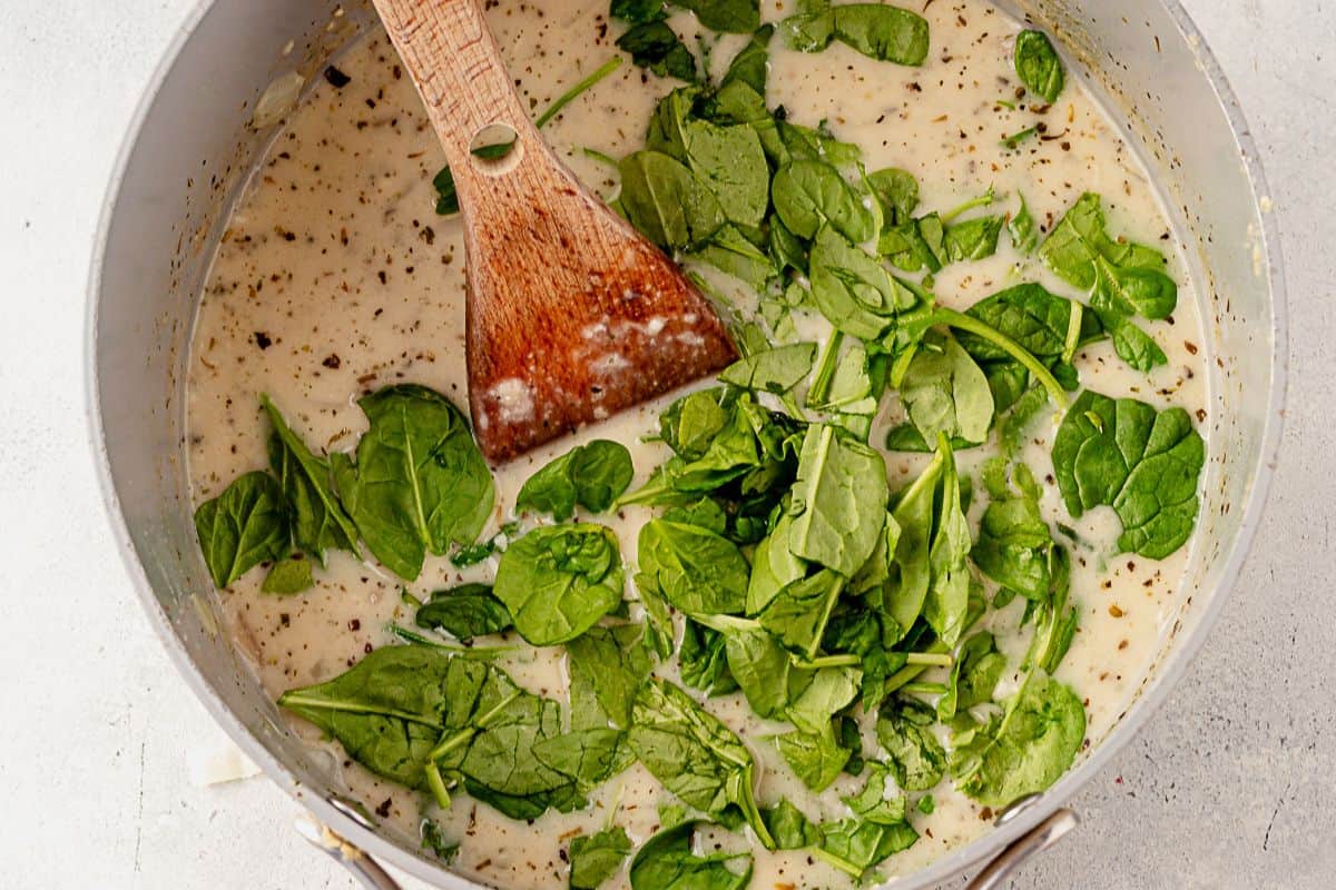 chopped spinach on top of a stock pot of creamy white lasagna soup