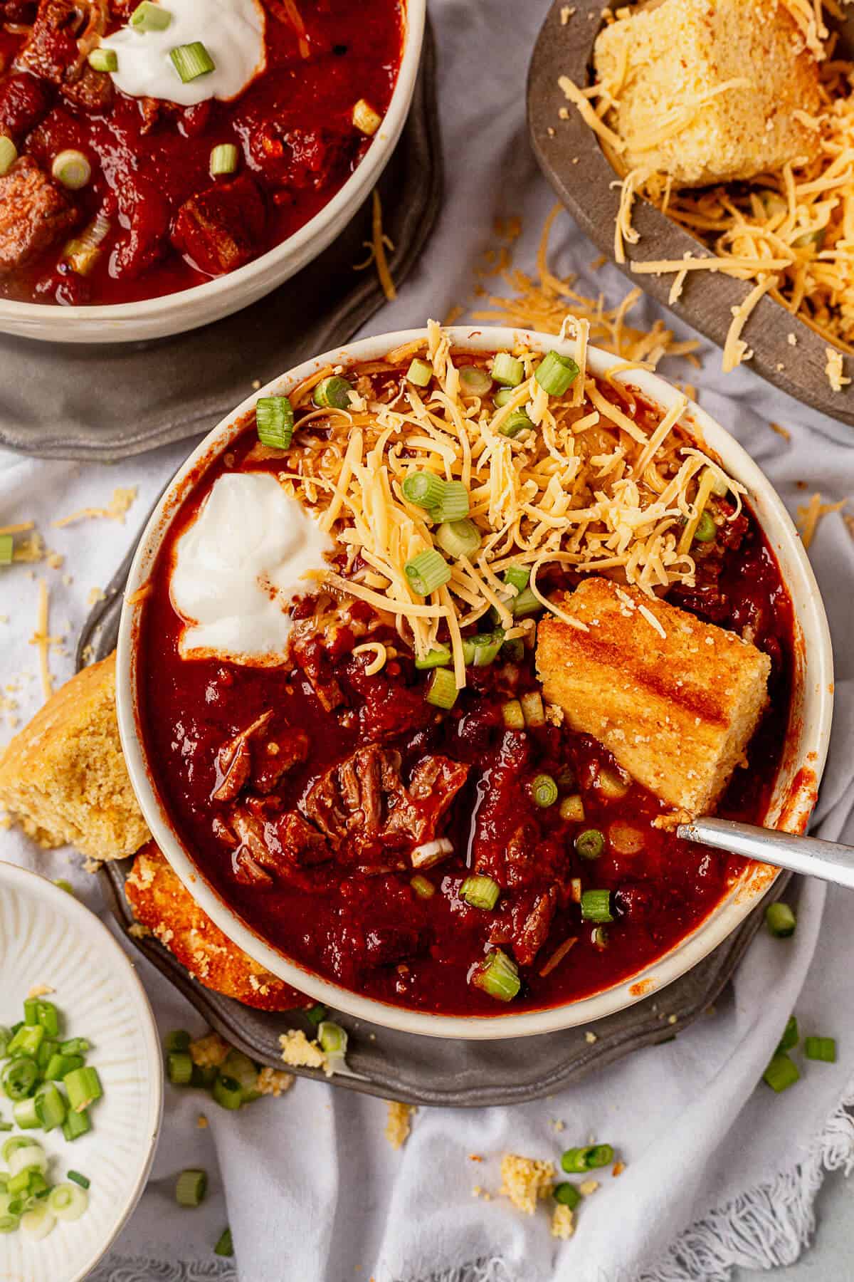 two bowls of crock pot steak chili with cheese, sour cream, and cornbread