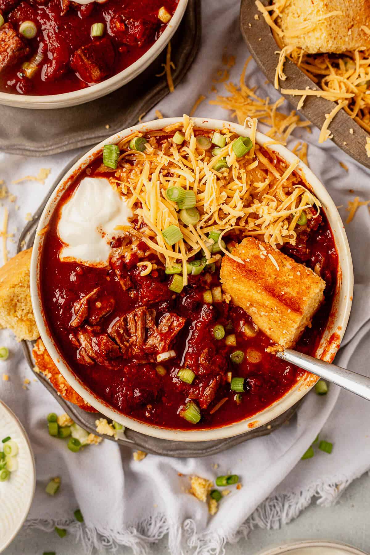 a spoon in a bowl of crock pot steak chili with cheese and sour cream