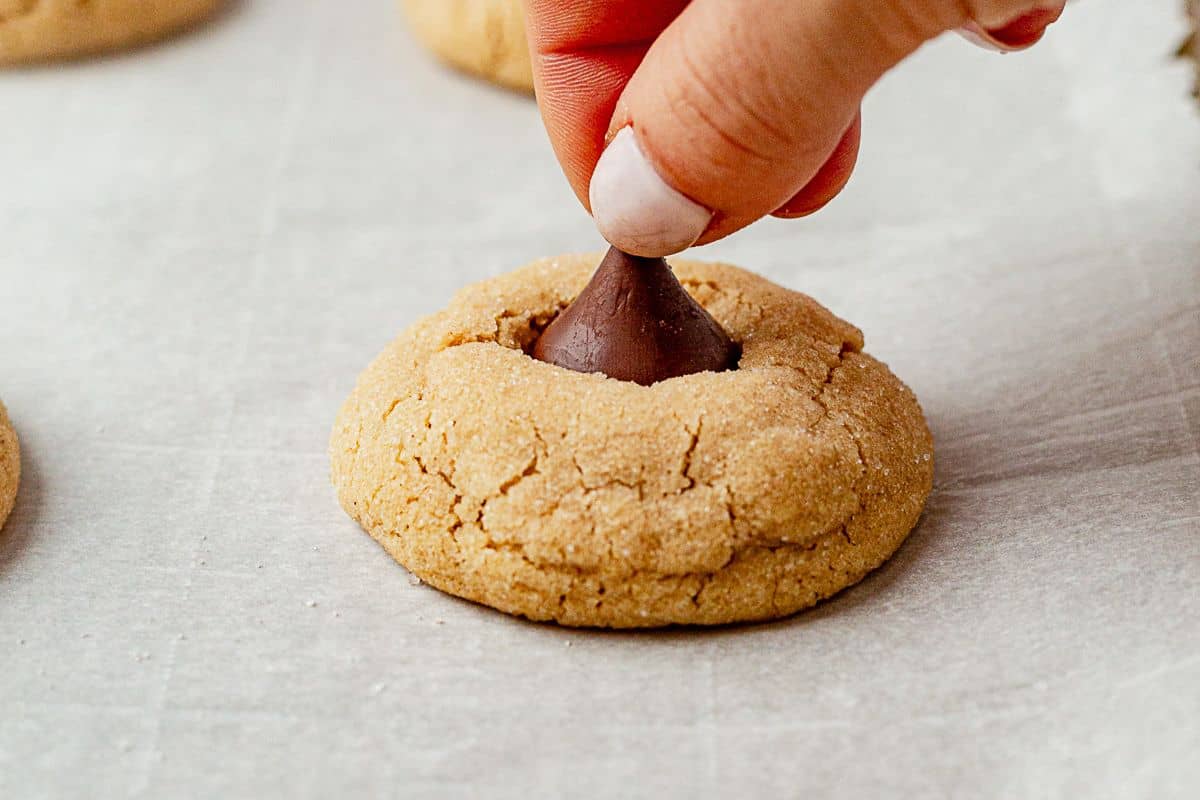 adding a hershey kiss on top of a freshly baked peanut butter cookie