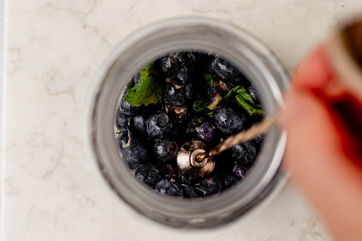 muddling blueberries and mint in a cocktail shaker