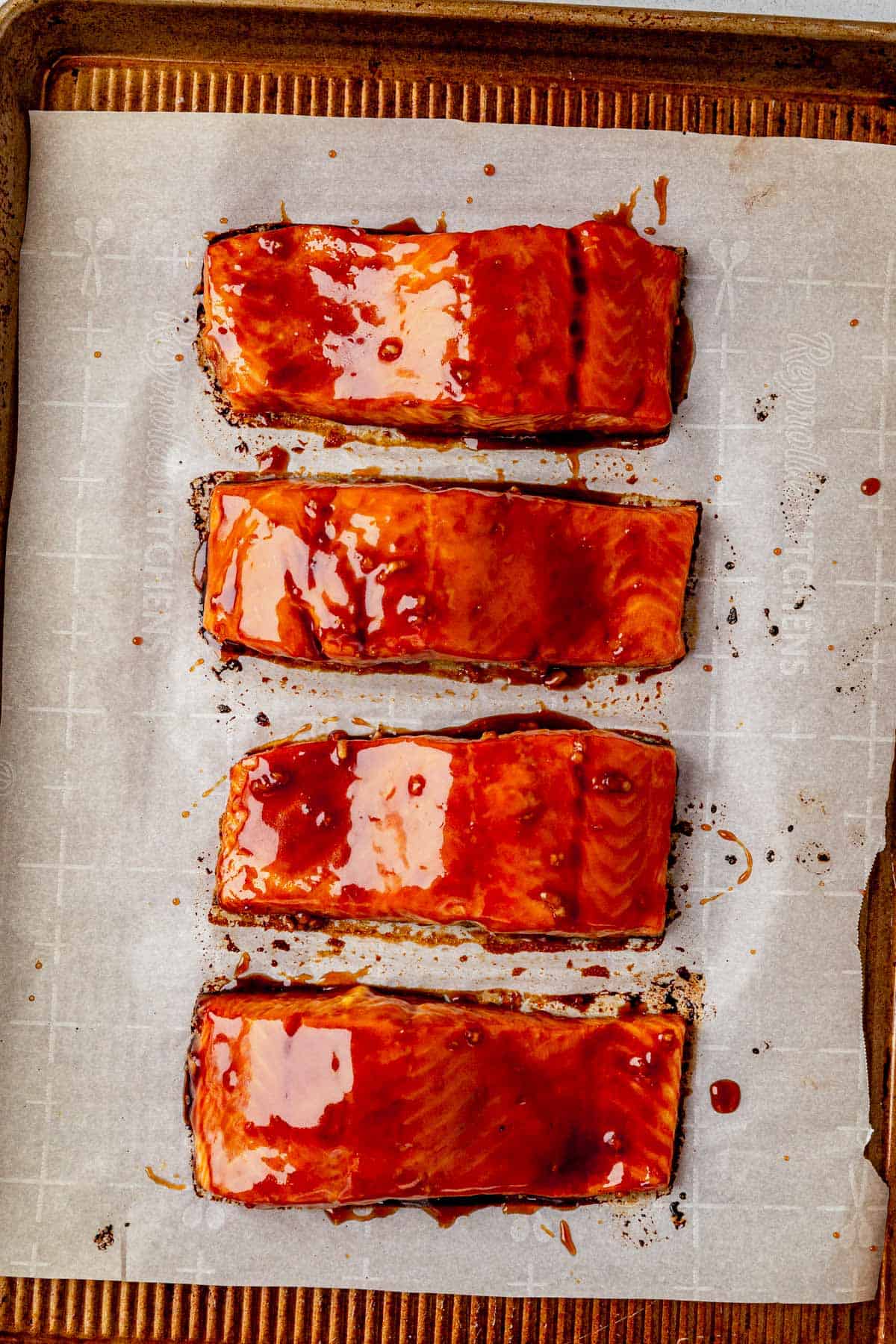 four honey sriracha salmon filets on parchment paper with extra glaze brushed on top