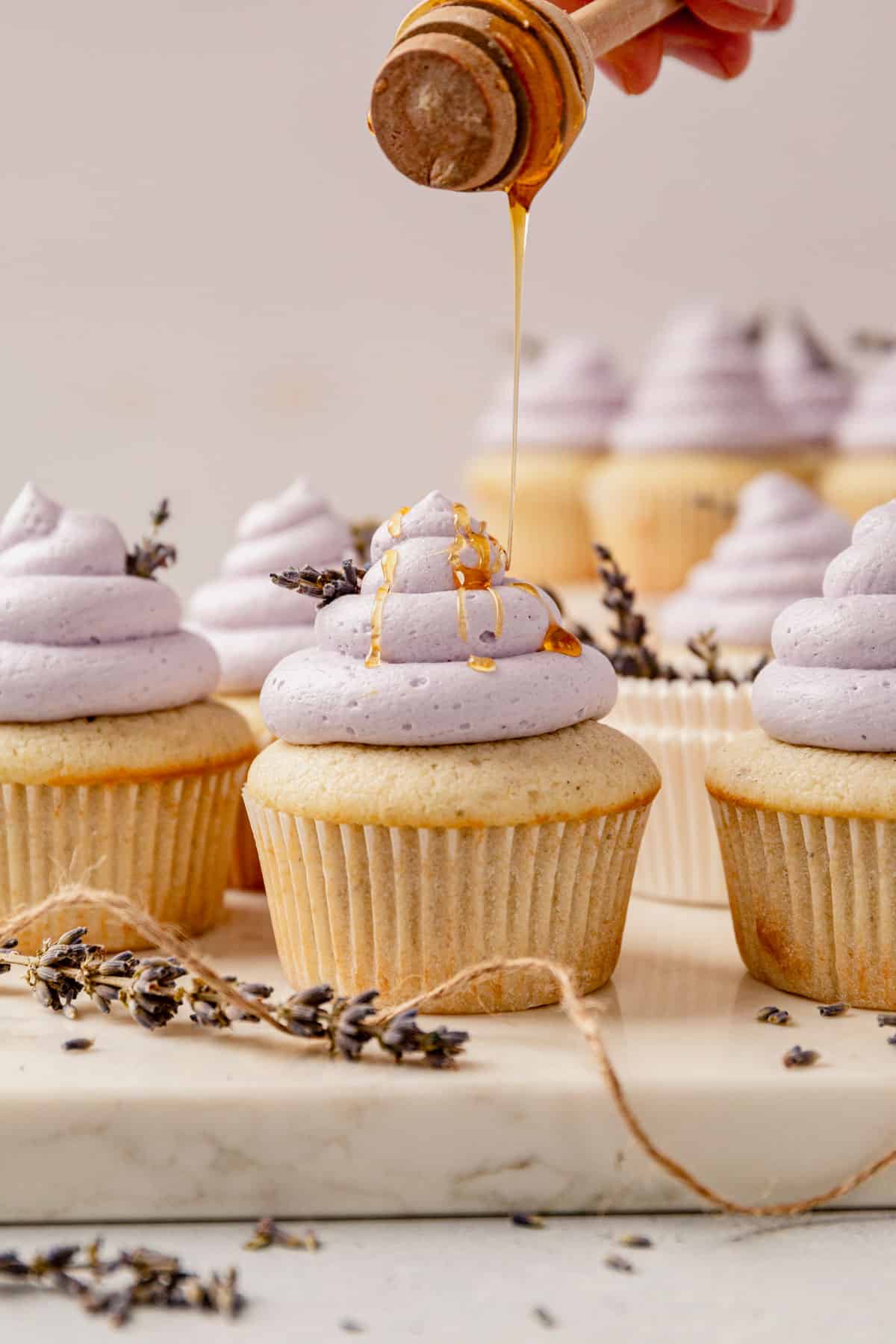 drizzling honey on top of a lavender cupcake with light purple frosting