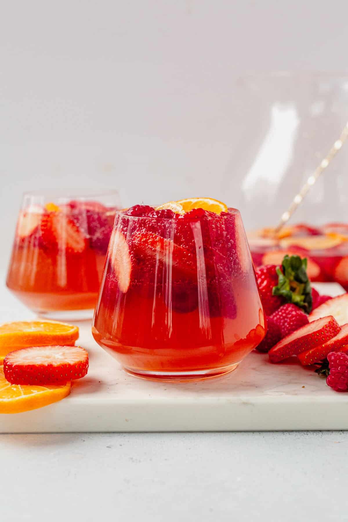 two wine glasses full of moscato sangria, berries, and oranges on a countertop