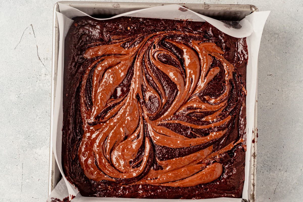 melted nutella swirled on top of brownie batter in a metal pan