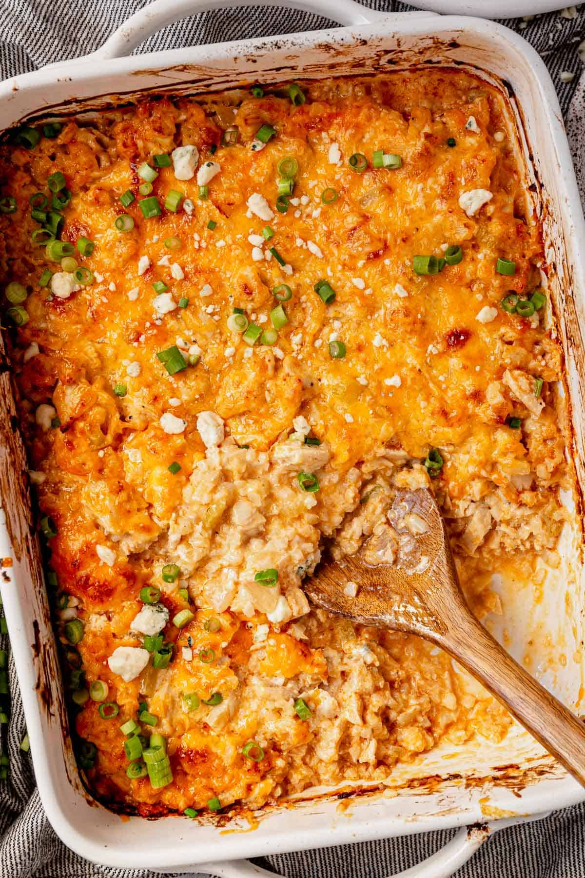 casserole pan of buffalo chicken casserole with a portion dug out with a wooden spoon