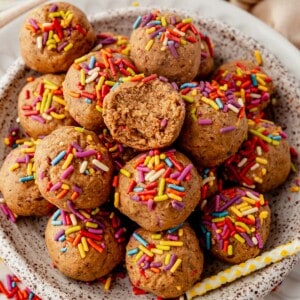 a plate of cake batter protein balls with a bite missing from the top one