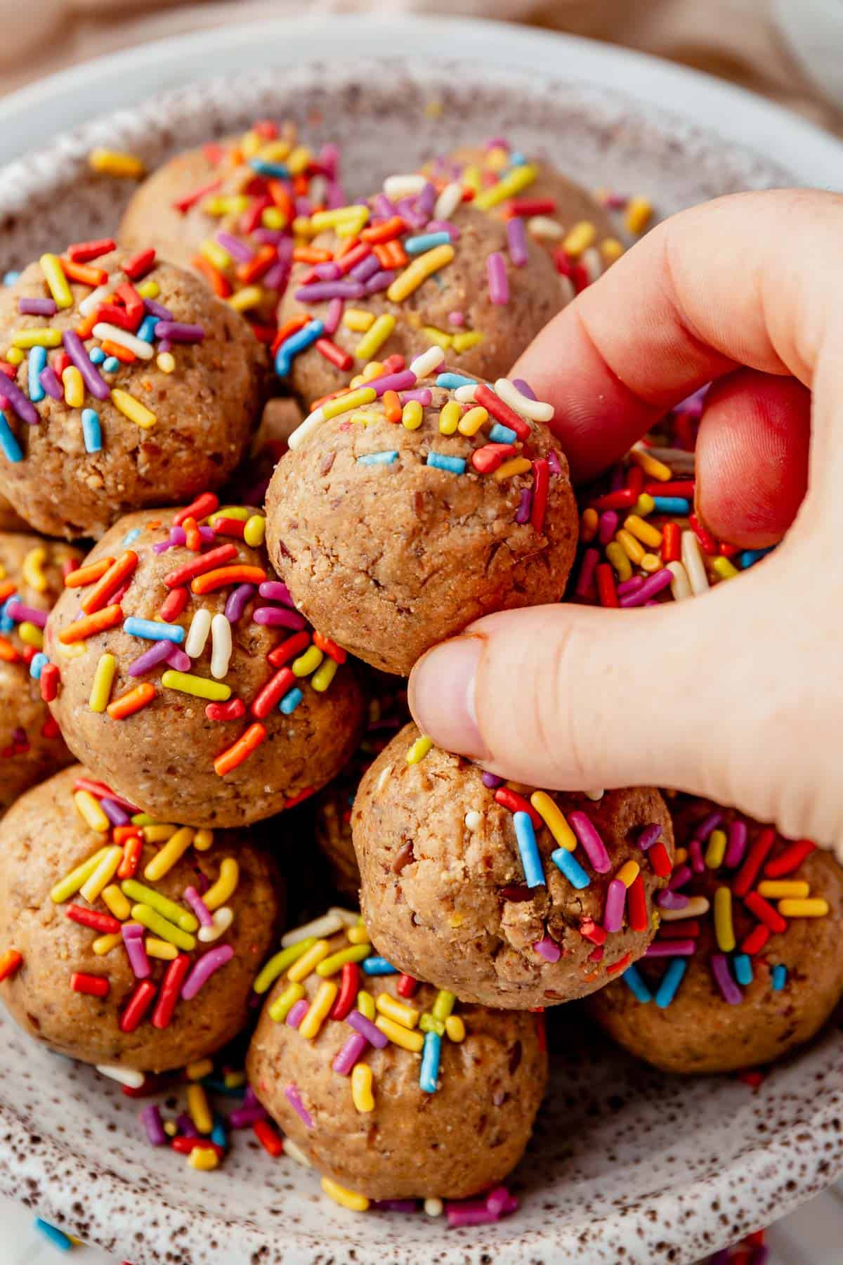 picking a cake batter protein ball off the top of a pile