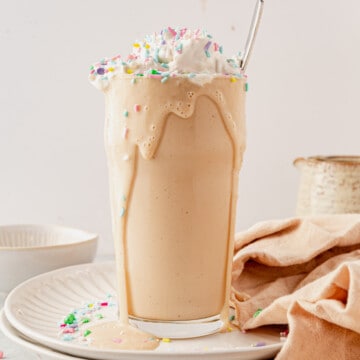 a cake batter protein shake with the shake running down the side and whipped cream and sprinkles on top