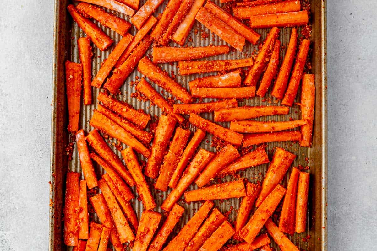 uncooked carrot fries in seasoning on a sheet pan