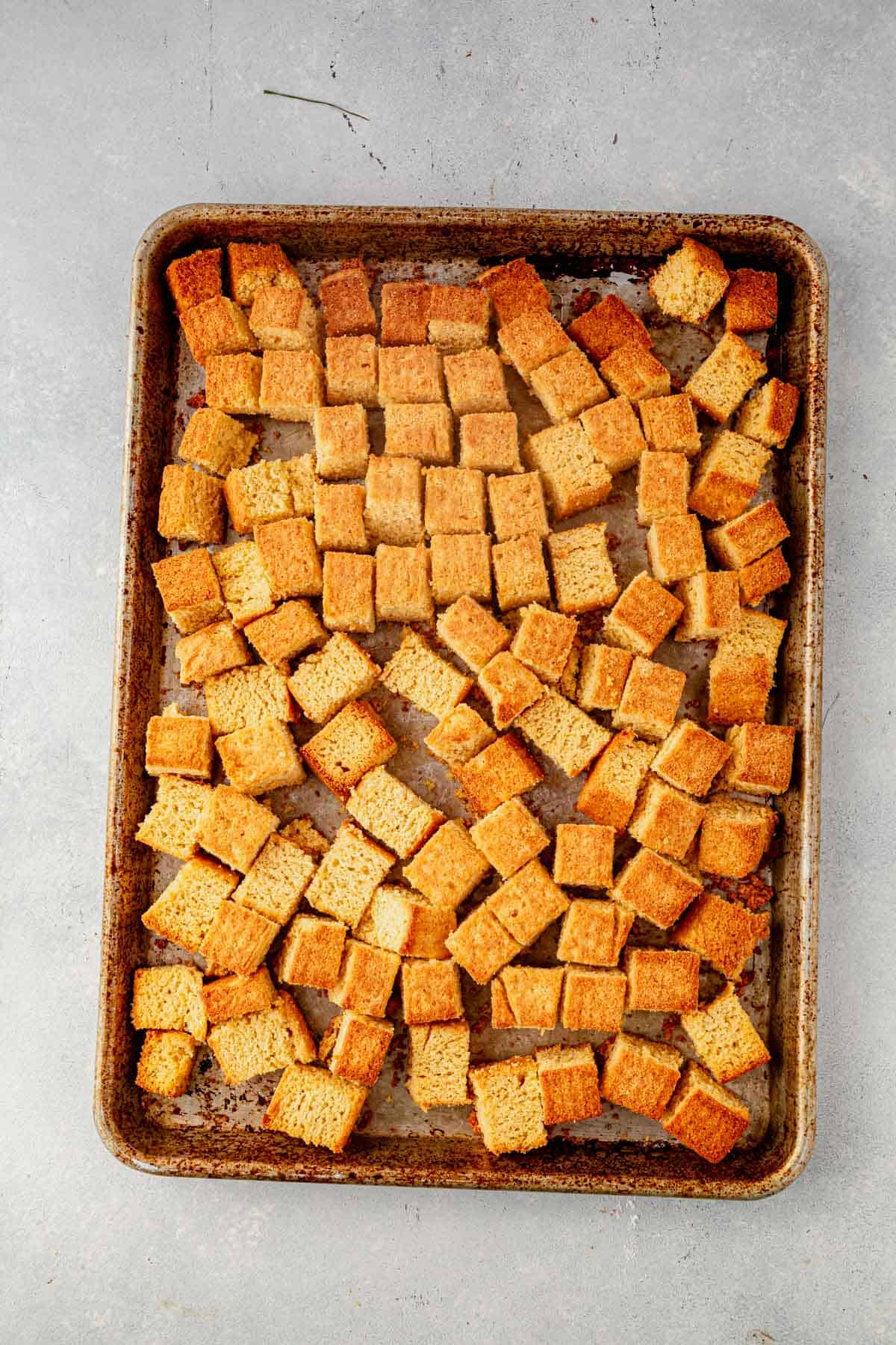 cubed cornbread drying out on a large sheet pan.