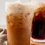 a tall glass of ice, root beer, rum, and cream mixed together with a stir stick inside sitting on a counter in front of another root beer cocktail in a tall glass with ice