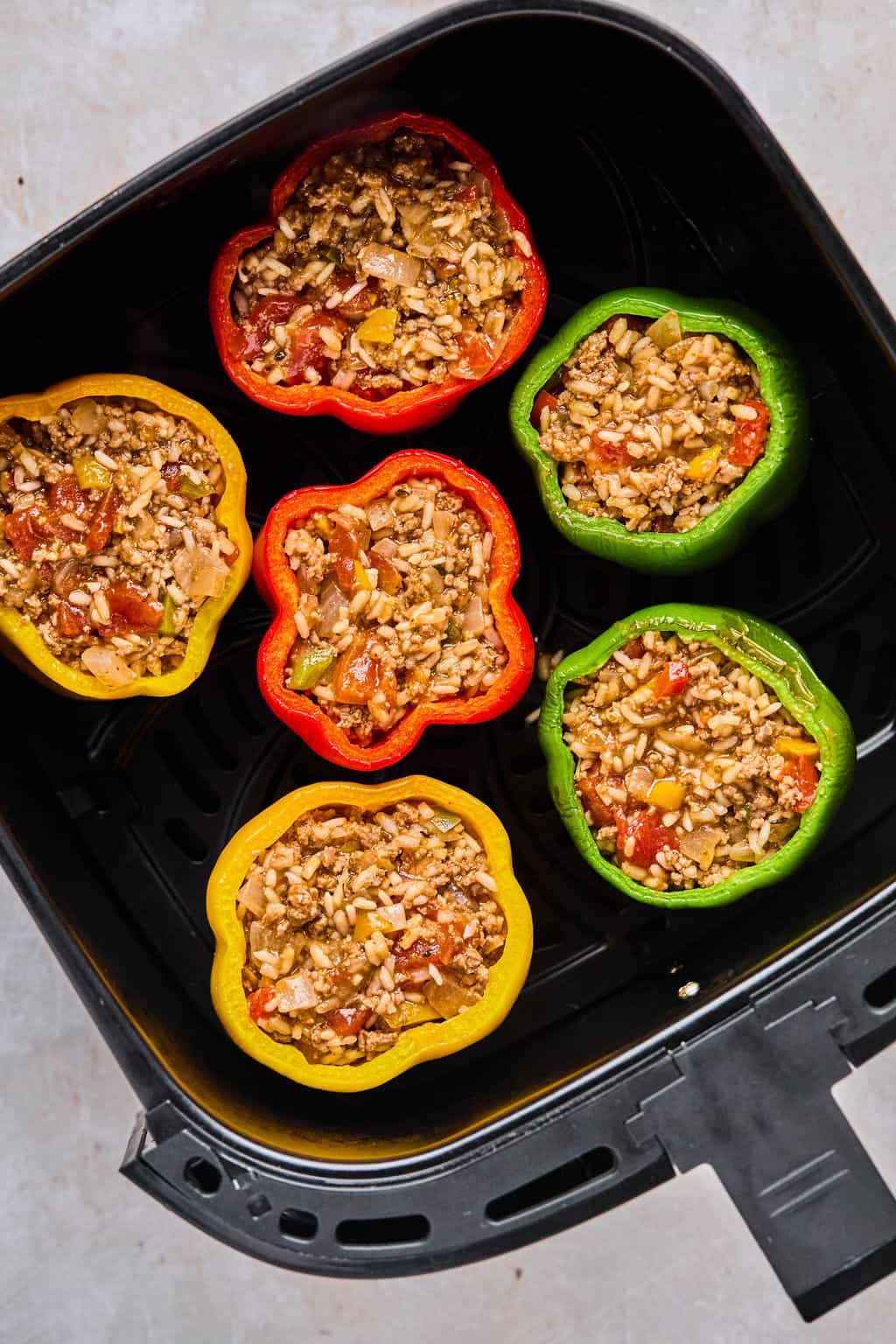 stuffed peppers filled with beef and rice in the basket of an air fryer.