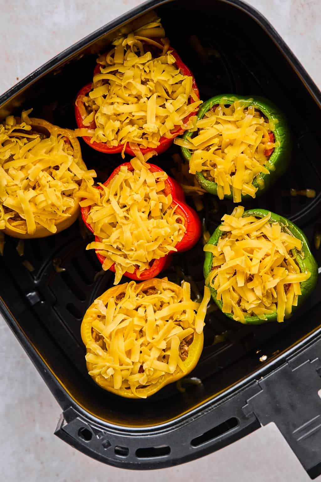 air fryer stuffed peppers in an air fryer basket with shredded cheese on top