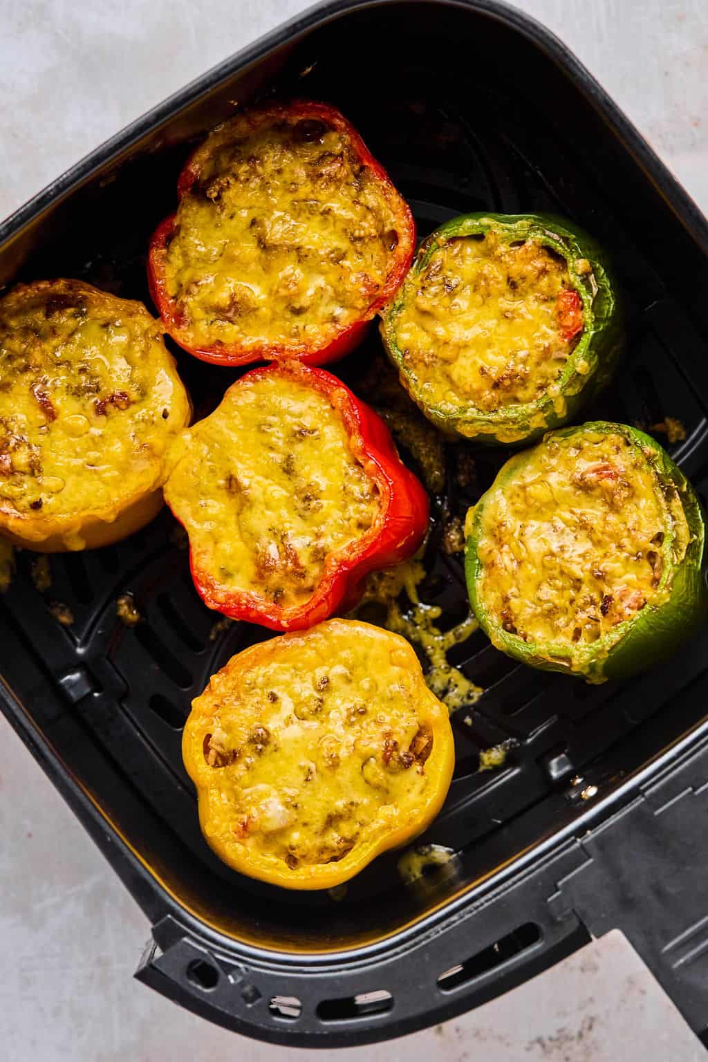 air fryer stuffed peppers topped with cheese in the air fryer basker.