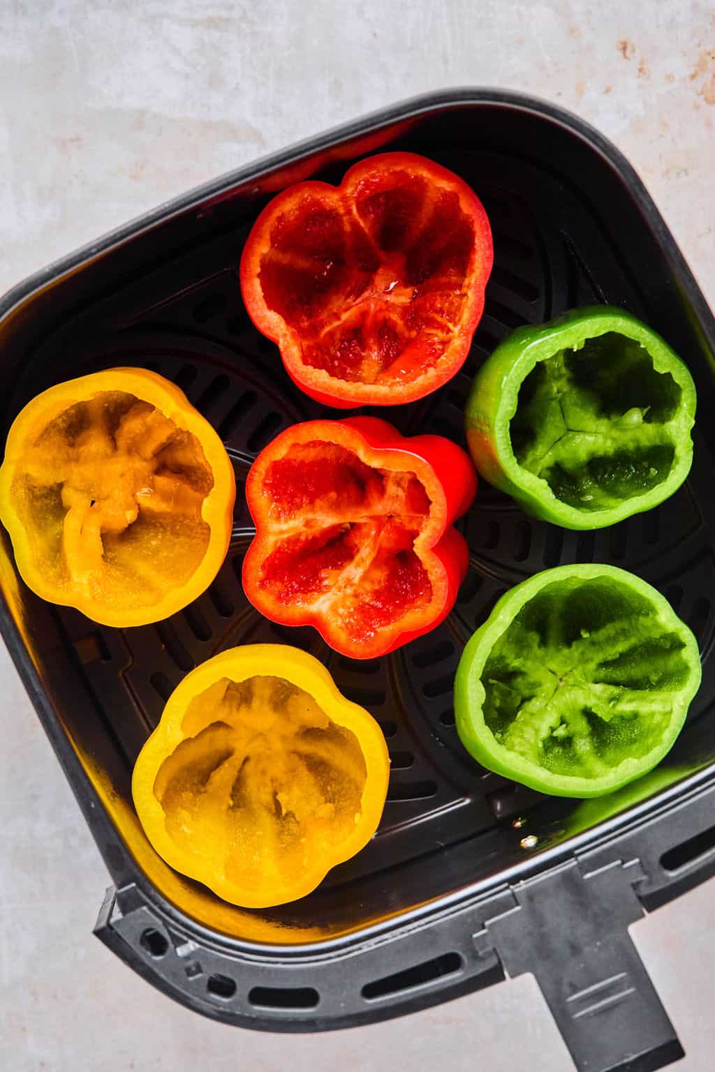 bell peppers with the tops cut off in an air fryer basket.