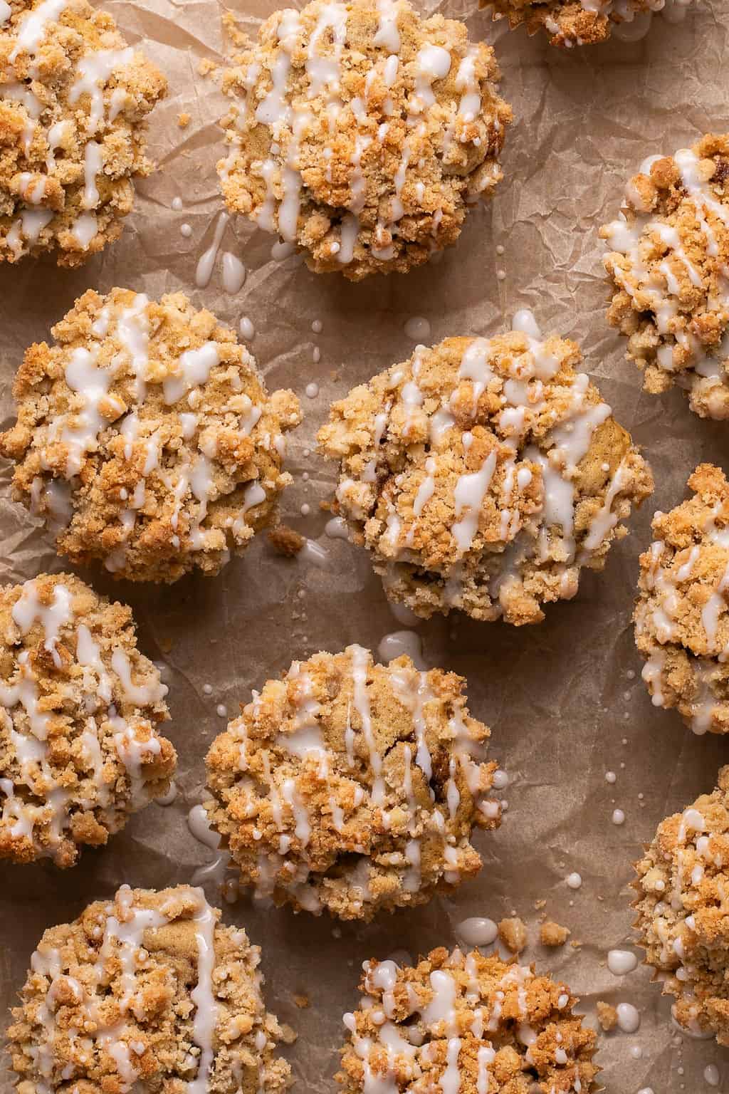 Baked coffee cake muffins arranged on a sheet of parchment paper. Each muffin is golden brown with a crunchy streusel top and drizzled with a sweet white glaze.