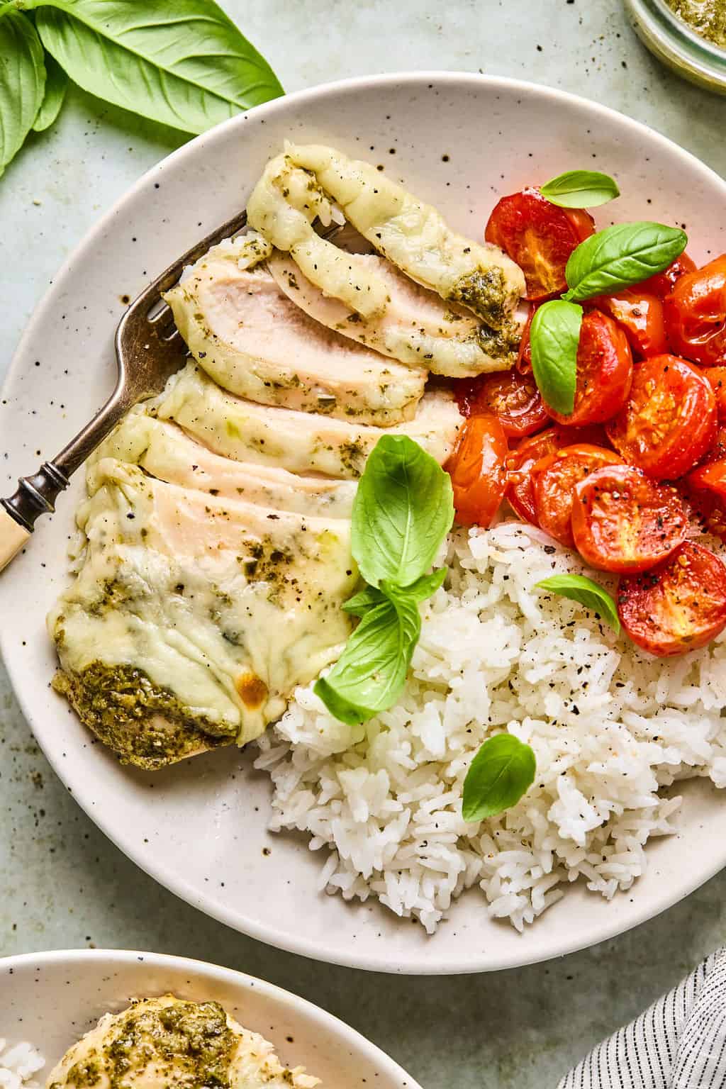sliced pesto chicken on a plate with roasted tomatoes and rice.