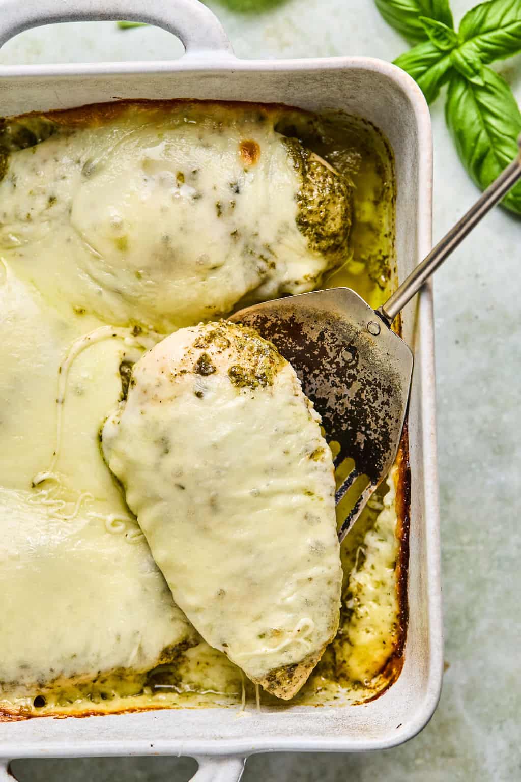scooping a piece of pesto baked chicken from a baking dish.