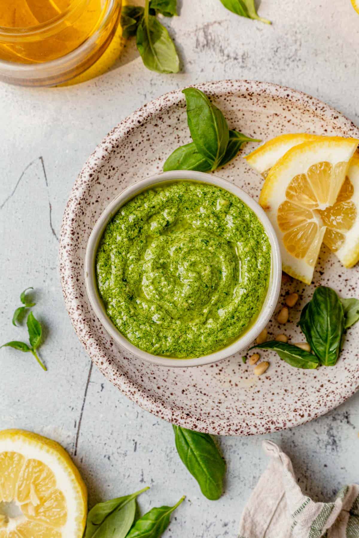 a bowl of homemade basil pesto on a plate with lemon and basil leaves