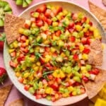 A plate of vibrant fruit salsa made with diced kiwi, strawberries, and mango, garnished with fresh herbs, and served alongside crispy cinnamon sugar tortilla chips.