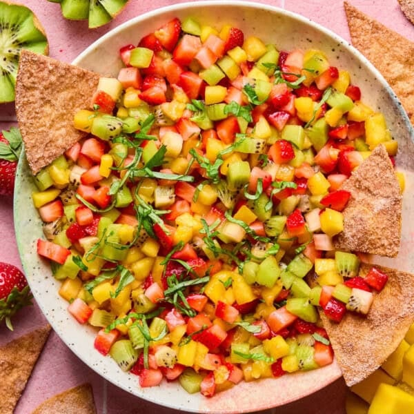 A plate of vibrant fruit salsa made with diced kiwi, strawberries, and mango, garnished with fresh herbs, and served alongside crispy cinnamon sugar tortilla chips.