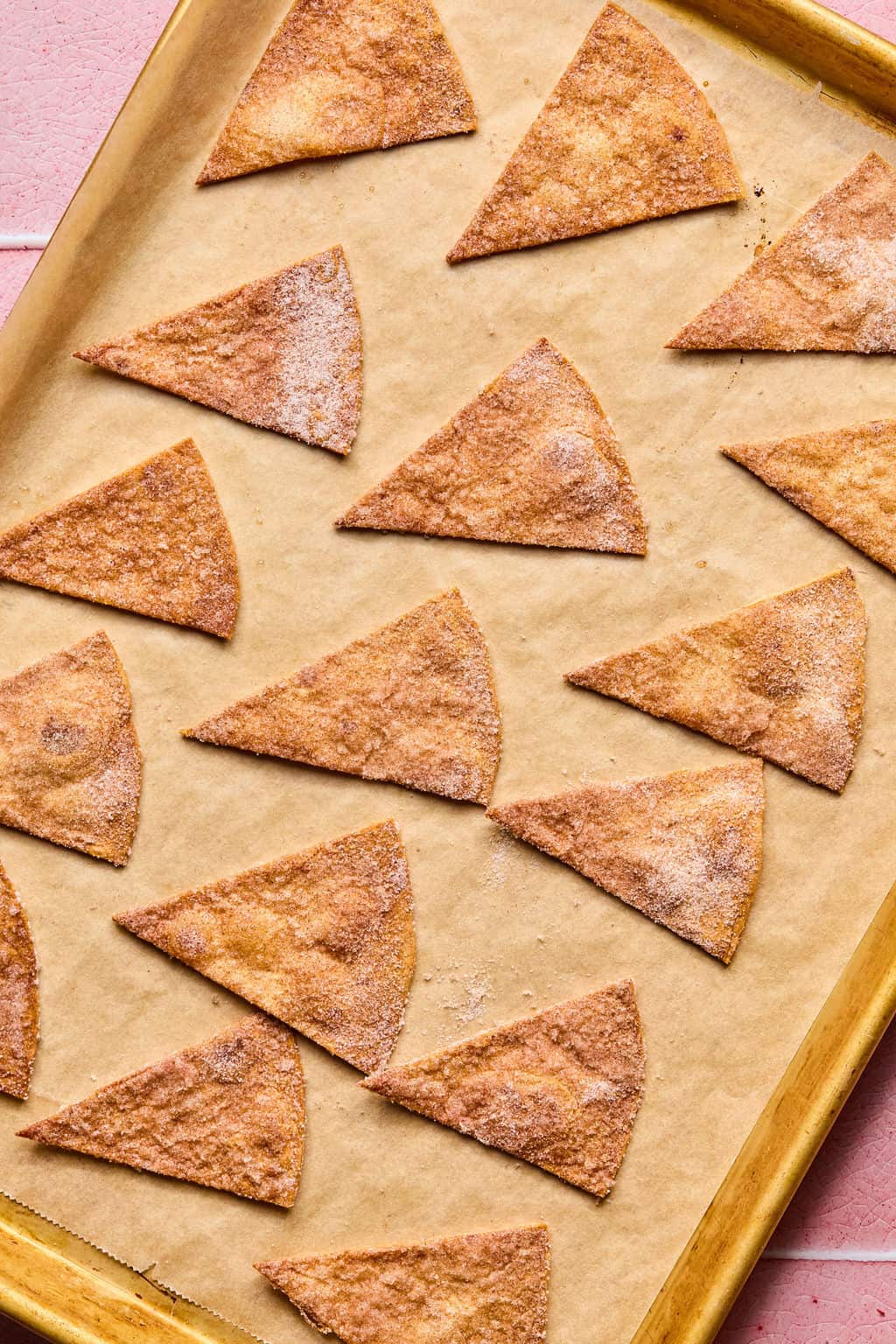 Baked cinnamon sugar tortilla chips arranged in a single layer on a parchment-lined baking sheet. These golden brown, triangular chips pair perfectly with fresh fruit salsa for a delightful snack or dessert.