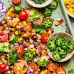 sweet potato nachos on a sheet pan with cilantro, jalapeno, avoacado, and tomatoes.