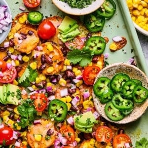 sweet potato nachos on a sheet pan with cilantro, jalapeno, avoacado, and tomatoes.