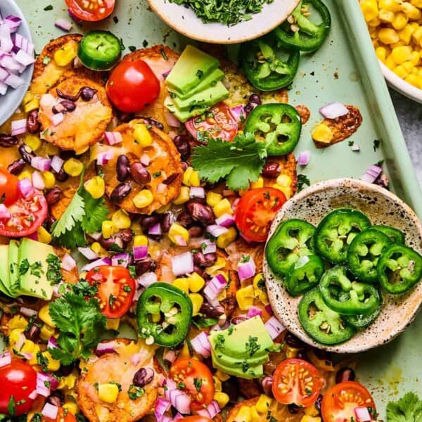 sweet potato nachos on a sheet pan with cilantro, jalapeno, avoacado, and tomatoes.