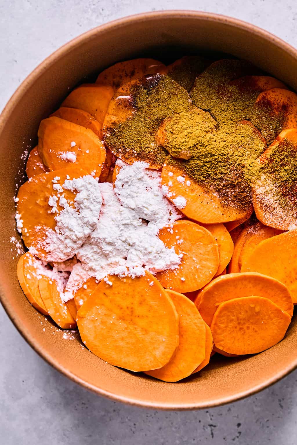 sweet potatoes sliced into rounds and tossed in a bowl with spices.