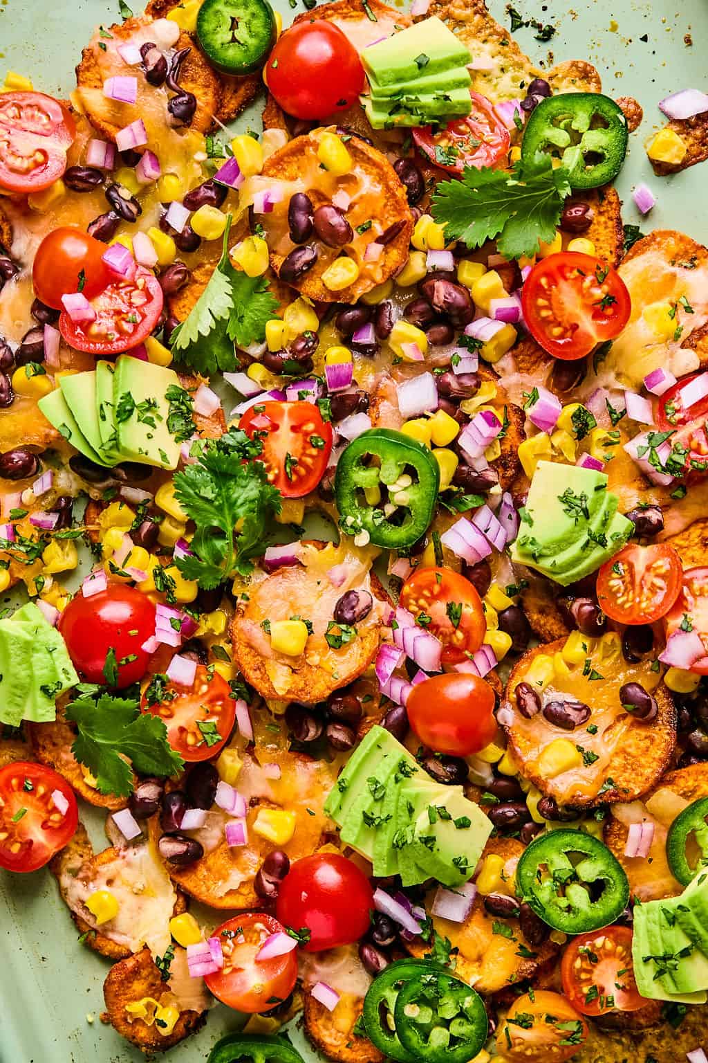 a tray of sweet potato nachos topped with tomato, avocado, and cilantro.