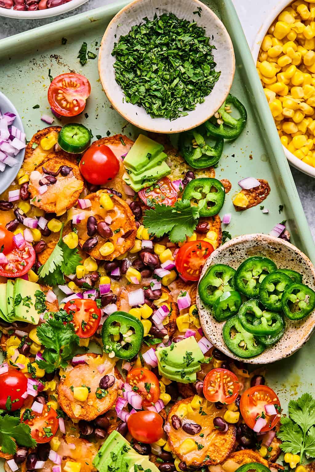 sweet potato nachos on a sheet pan with chopped cilantro and jalapeno in a bowl.