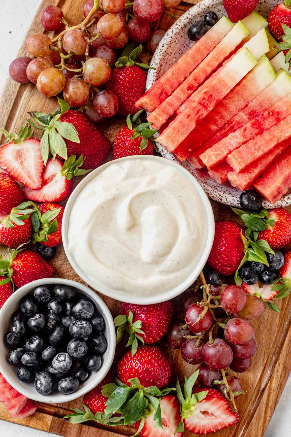 yogurt fruit dip on a platter with watermelon, grapes, strawberries, and blueberries