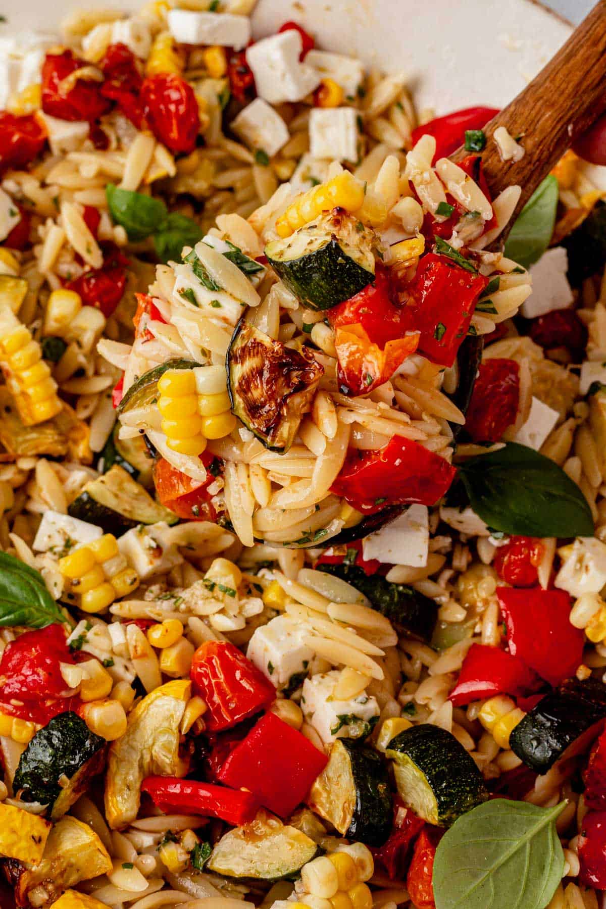 scooping roasted vegetable pasta salad out of a serving bowl