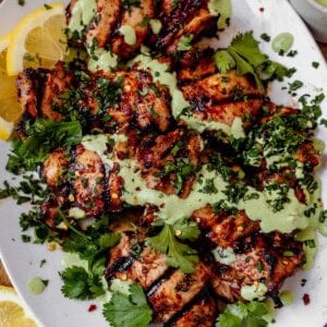 harissa chicken on a serving platter with cilantro and yogurt sauce