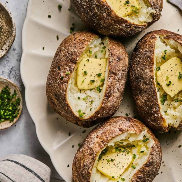 air fryer baked potatoes on a plate with butter and chives.