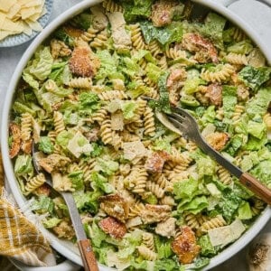 caesar pasta salad in a serving bowl with a salad spoon and fork.